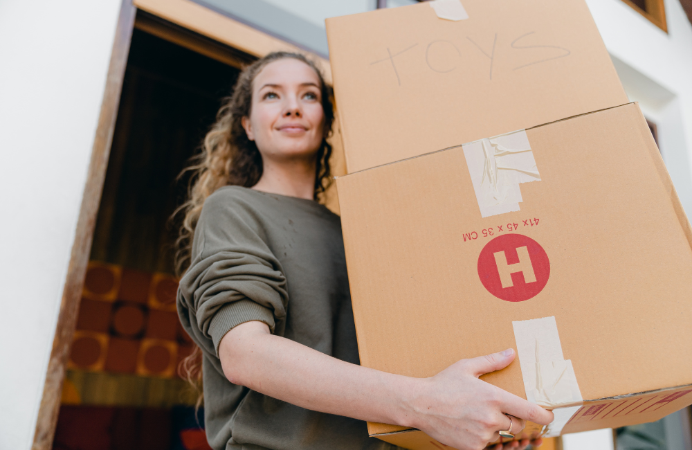A women carrying a couple of moving boxes out the front door.