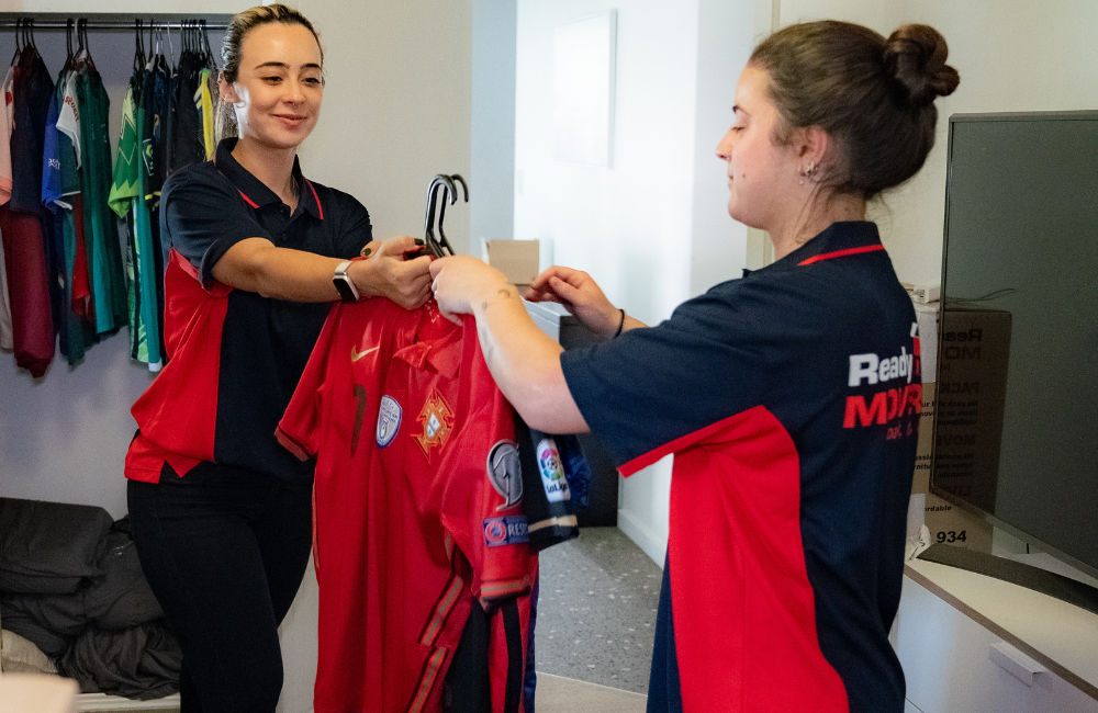 Two Ready Movers packers passing each other shirts to pack into a port-a-robe.