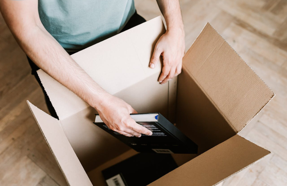 A person kneeling next to a box and placing books into it. 