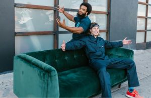 Two removalist men sitting on an emerald green velvet couch out in the street.