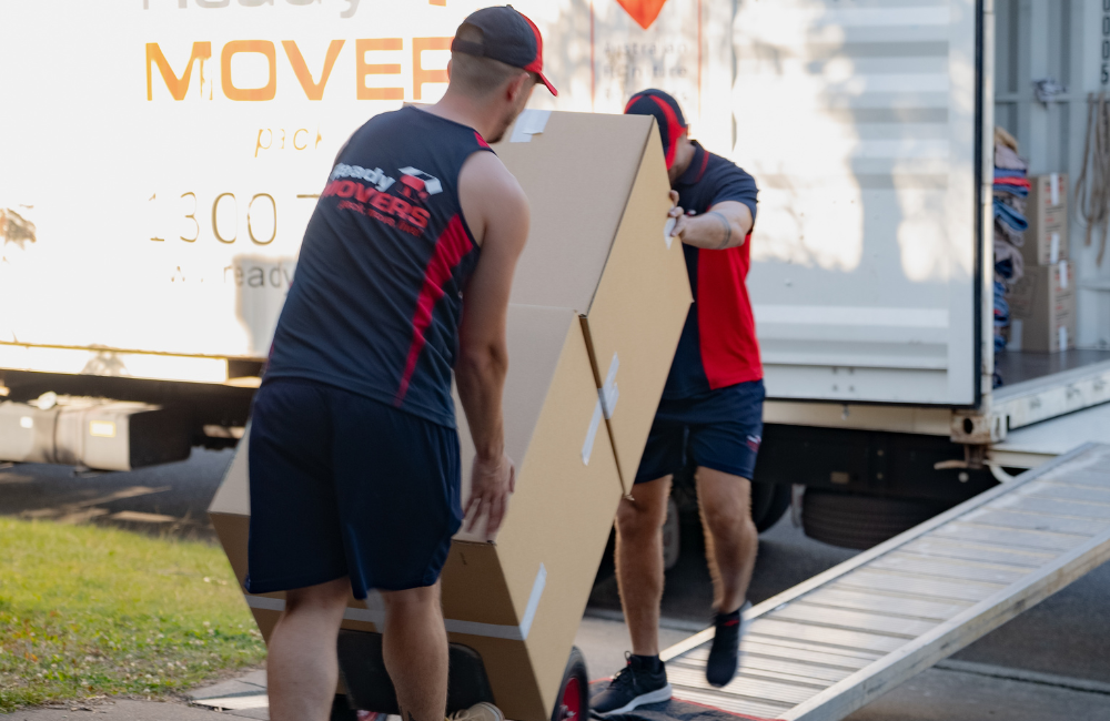 Two Ready Movers removalists wheeling a stack of boxes out to the truck. 
