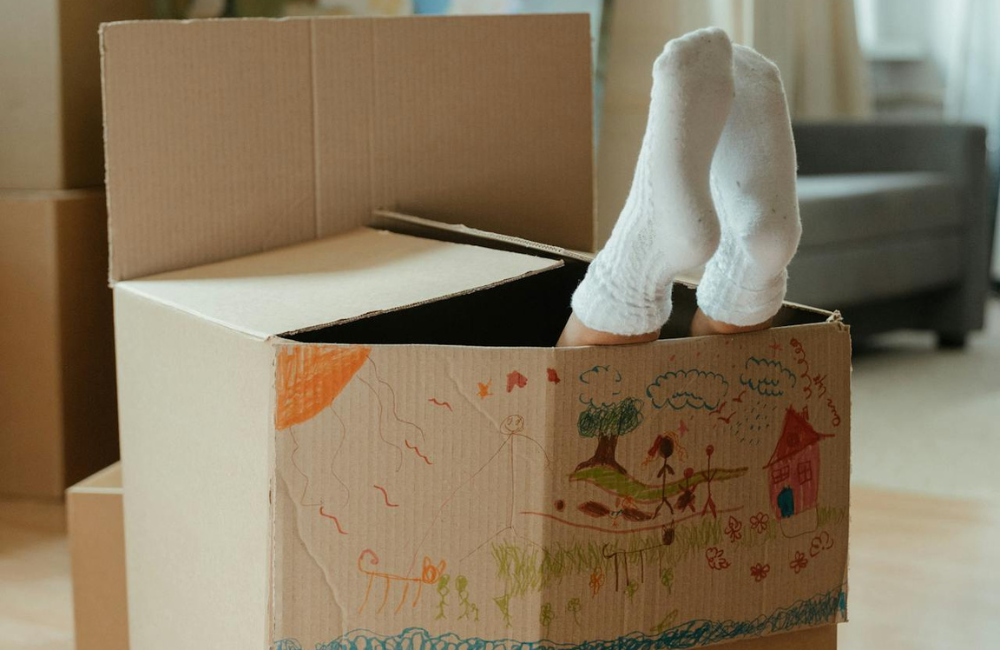A child's feet with cotton white socks on poking out the top of a drawn on moving box.